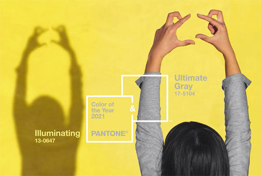 Person forming a heart shape with their hands in front of a yellow background, showcasing the Pantone 2021 Colors of the Year, Illuminating (13-0647) and Ultimate Gray (17-5104).