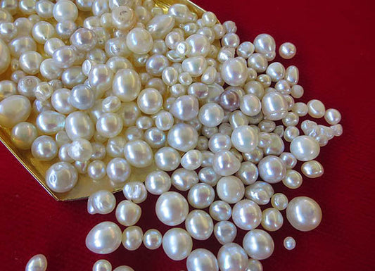 A collection of lustrous white pearls of various sizes, spilling from a golden tray against a red background.