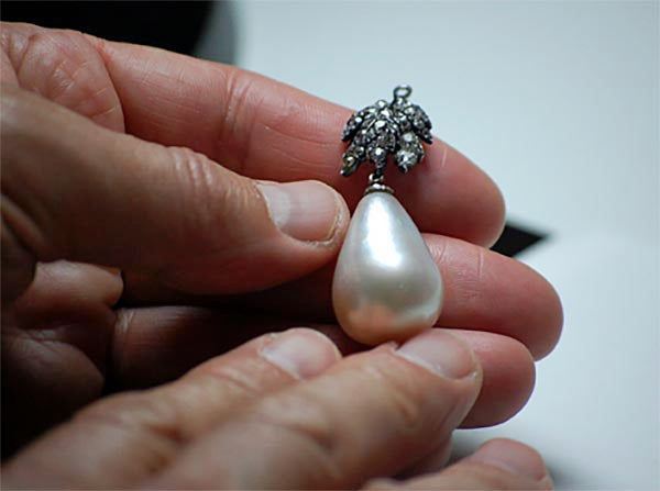 A hand holding a vintage pearl earring with a diamond-studded top, showcasing its elegant design and luxurious craftsmanship.