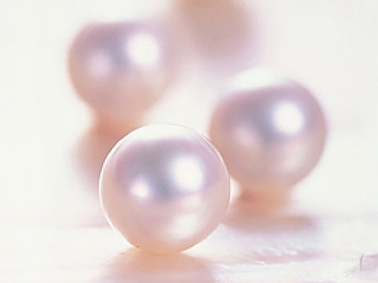 Close-up of several lustrous white pearls placed on a soft, light-colored surface, showcasing their smooth and shiny texture.
