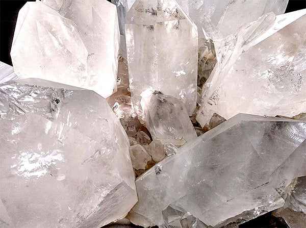 Cluster of large, clear quartz crystals with sharp edges, reflecting light, creating a crystalline and glossy appearance.