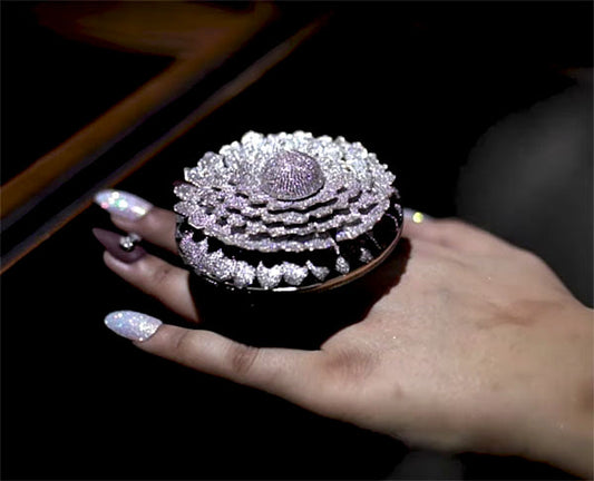 A close-up of a hand holding a luxurious diamond flower-shaped brooch with intricate layers of diamonds, sparkling with a shimmering design.