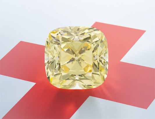 A large cushion-cut yellow diamond displayed on a red cross background, showcasing its brilliant facets and clarity.