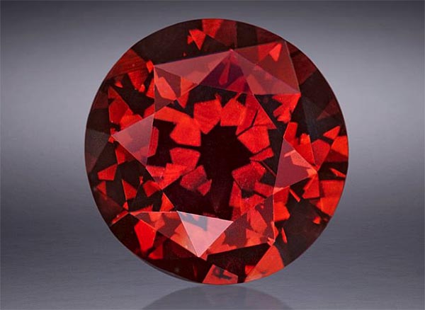 A stunning, round cut red garnet gemstone, showcasing its intricate facets and deep red color, reflecting light beautifully.
