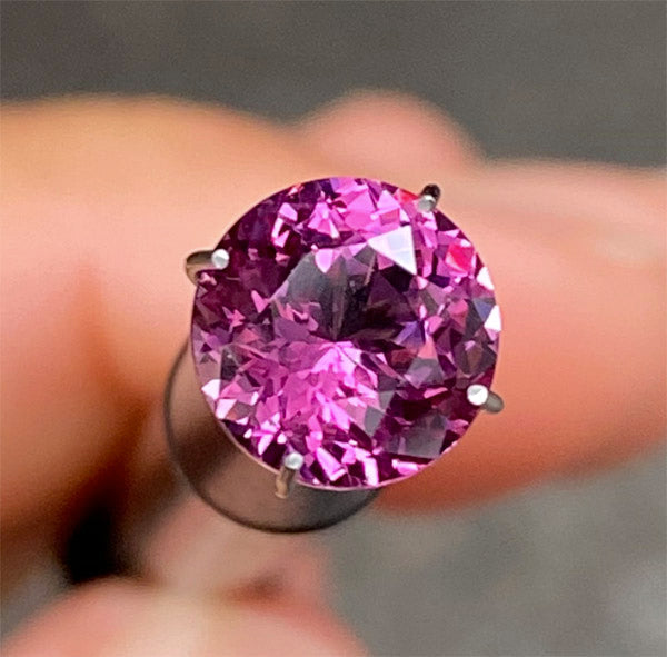 Close-up of a round pink gemstone being held with fingers, showcasing its clarity and vibrant color.