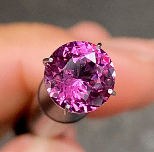 Close-up of a round pink gemstone being held with fingers, showcasing its clarity and vibrant color.