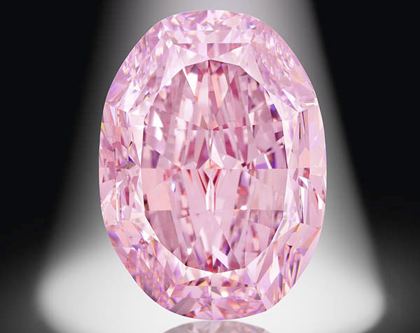 Large oval-shaped pink diamond, reflecting light with intricate facets, set against a dark background with a spotlight highlighting its brilliance.