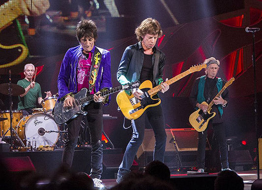 The Rolling Stones performing live on stage with Mick Jagger, Keith Richards, Ronnie Wood, and Charlie Watts playing guitar, drums, and bass during a concert.