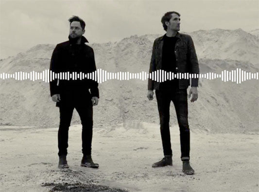 Black and white photo of two musicians standing in front of a mountainous backdrop with a soundwave graphic overlay, representing music and sound.