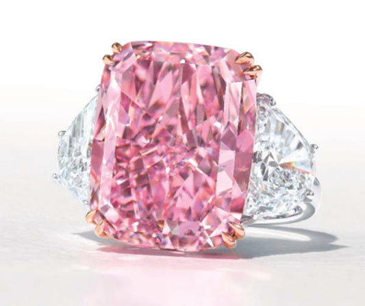 Large pink cushion-cut diamond ring with two white trapezoid diamonds on either side, set in a platinum band with rose gold accents.