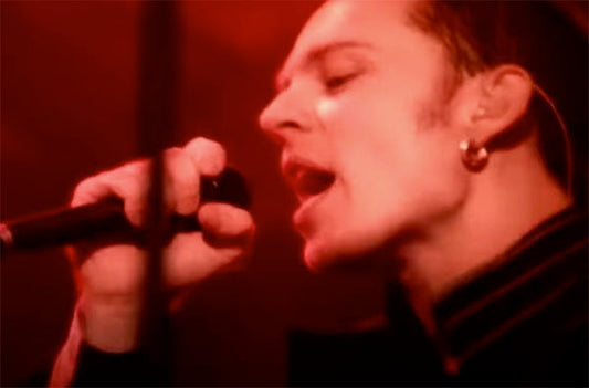 Close-up of Scott Weiland performing on stage, singing into a microphone with dramatic red lighting in the background.