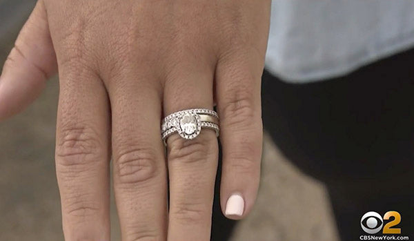 A close-up of a hand wearing a diamond engagement ring and wedding band set, featuring a central oval diamond surrounded by smaller diamonds on the bands.