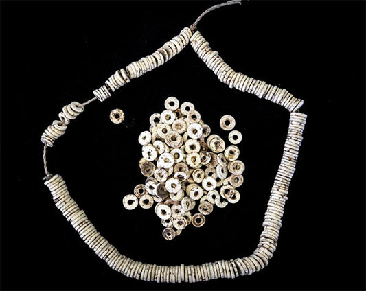 Close-up of a necklace made of white cylindrical beads, with a pile of similar beads arranged beside it. The beads are uniform in shape, and the image is set against a black background, highlighting the intricate design.