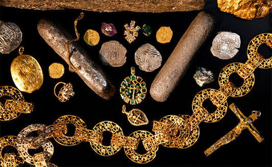 A collection of historical gold coins, jewelry, and artifacts including a gold chain, a cross pendant, and a variety of precious stones and ancient relics displayed on a dark background.
