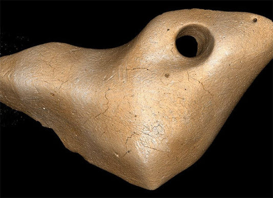 Close-up of an ancient stone bird-shaped object with a circular hole, believed to be a prehistoric artifact, highlighting cracks and texture.