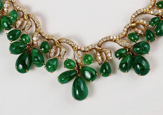 Close-up of an elegant necklace featuring green jade teardrop gemstones surrounded by small diamonds, set in a gold chain.