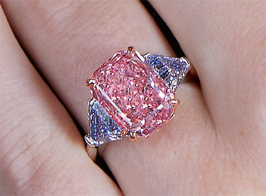 Close-up of a hand wearing a luxurious pink diamond ring with blue sapphire accents.