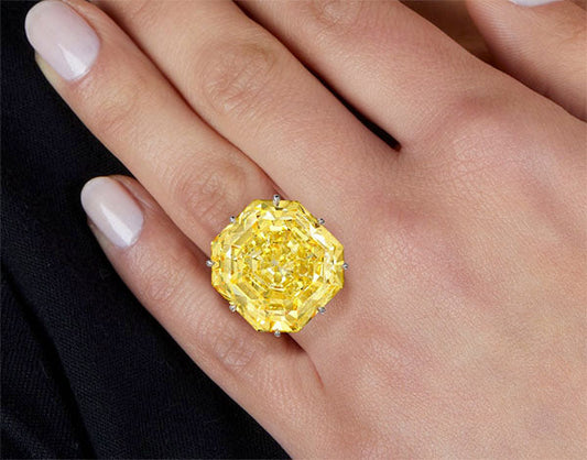 Close-up of a hand wearing a yellow diamond engagement ring with an octagonal cut, set in a silver band.