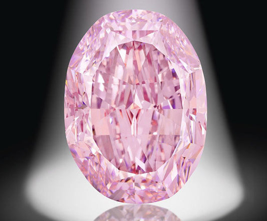 Close-up of a dazzling pink diamond with an oval shape, brilliantly cut to highlight its facets. The diamond is illuminated by a spotlight, creating a stunning display of light and color against a dark background.