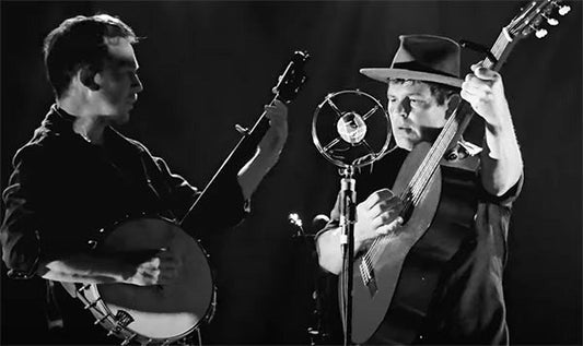 Two musicians performing on stage in black and white. One musician is playing the banjo, while the other is playing the guitar. 