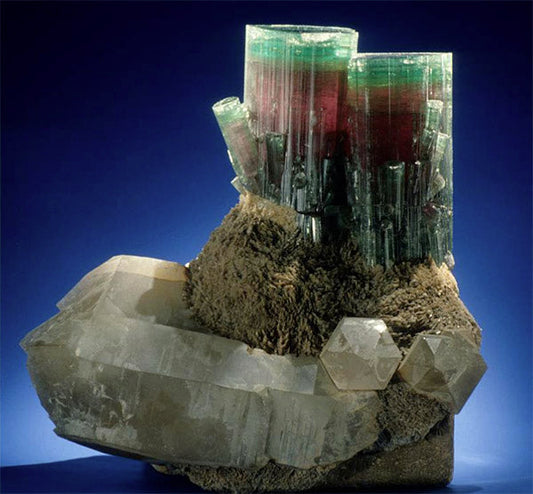 Close-up of a stunning mineral formation featuring green and red tourmaline crystals on a base of clear quartz, with a striking contrast between the vibrant colors of the tourmaline and the transparent quartz.