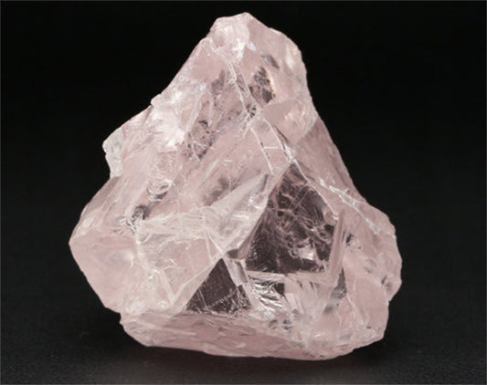 Close-up of a rough rose quartz crystal with clear, sharp edges and a pale pink hue, set against a dark background.