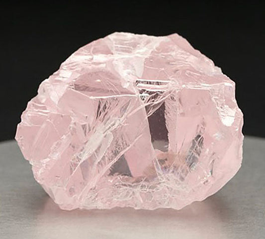 Close-up of a rough, uncut pink quartz crystal showcasing its natural shape and translucent edges.