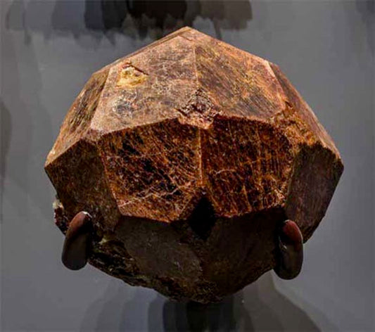 Large rough garnet crystal with distinct geometric facets displayed in a museum setting.