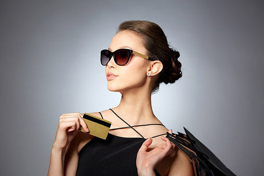Fashionable woman wearing sunglasses, holding a gold credit card and a shopping bag, exuding elegance and confidence.