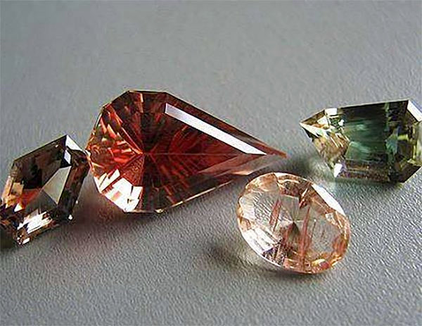 Collection of various colored gemstones, including pink, orange, and green, with different cuts and shapes, showcasing their brilliance and clarity.