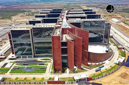 Aerial view of the Surat Diamond Bourse, a large modern building complex with reflective glass surfaces and landscaped grounds in Surat, India.