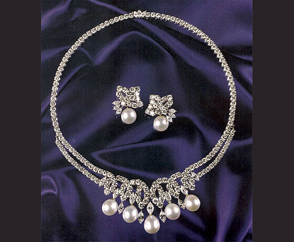 Elegant pearl necklace with diamond accents and matching earrings, displayed on a purple satin fabric backdrop.