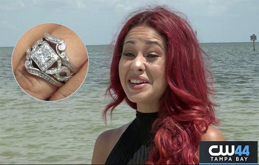 Smiling woman with red hair, wearing a black top, standing by the beach with a close-up image of her diamond engagement ring featuring a large square-cut diamond and intricate band design.