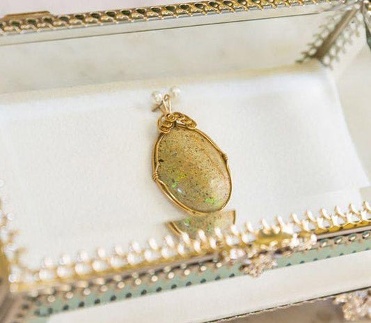 Elegant gold pendant with a large opal stone displayed in a jewelry box with decorative details.