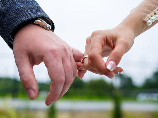 Close-up of a man and woman holding hands with a focus on wedding rings, symbolizing love and commitment outdoors.