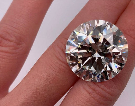Close-up of a sparkling large round-cut diamond ring on a finger, showcasing its brilliant facets and clarity against a neutral background.