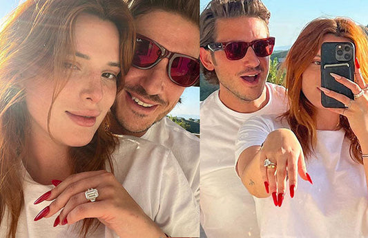 Celebrity couple sharing a selfie, showing off an engagement ring with a large diamond, both wearing sunglasses in a bright outdoor setting.