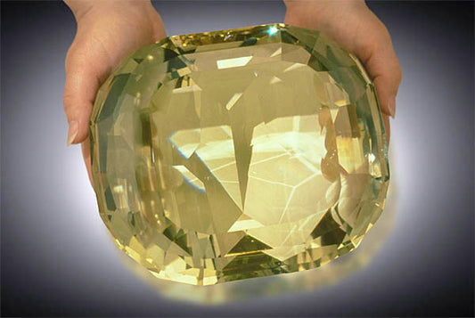 Large yellow sapphire gemstone being held, showcasing its crystal clarity and size.