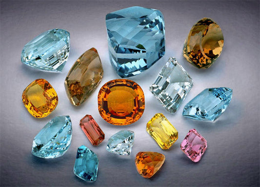 Collection of colorful gemstones, including blue, yellow, orange, pink, and clear crystals, arranged in various cuts and shapes.