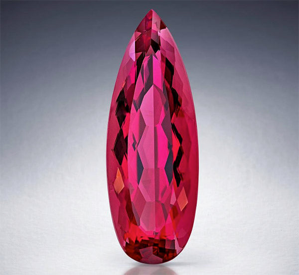 Close-up of a stunning pink marquise-shaped gemstone with brilliant facets, showcasing its vivid color and clarity against a simple gradient background.