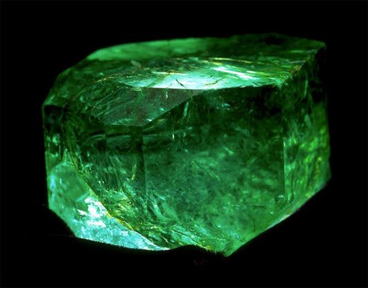 Large, raw emerald gemstone displaying vibrant green color and sharp, angular facets.