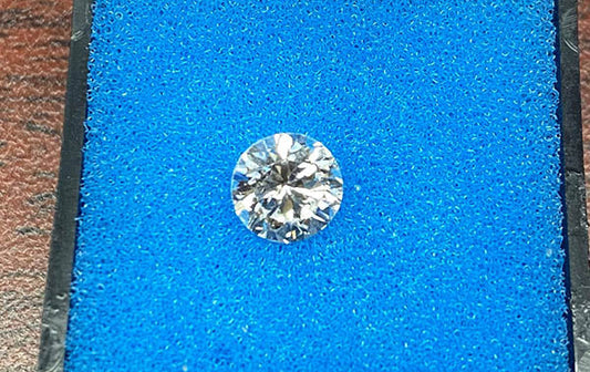 Close-up of a round brilliant cut diamond on a blue background, showcasing its clarity, brilliance, and reflective facets.