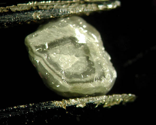 Close-up view of a raw diamond crystal, showcasing its unique shape and surface texture with sharp edges and a translucent appearance.