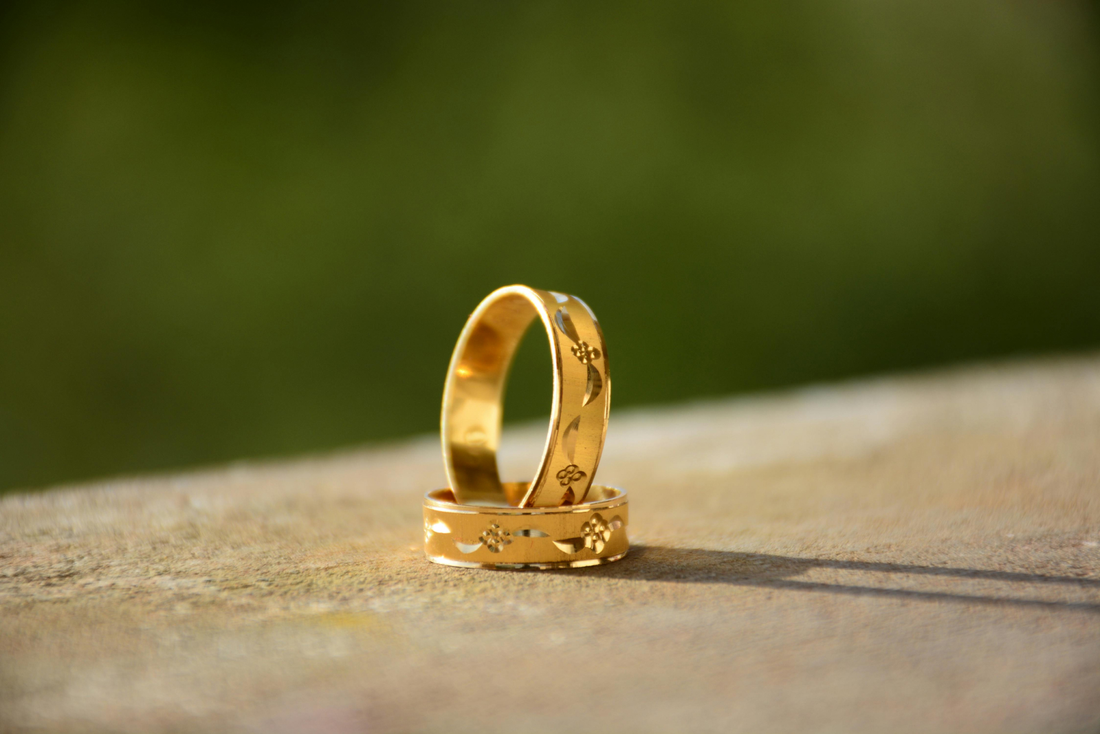 Two elegant gold wedding bands with floral engravings placed on a surface, capturing intricate design details and natural light.