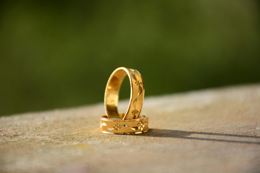 Two elegant gold wedding bands with floral engravings placed on a surface, capturing intricate design details and natural light.
