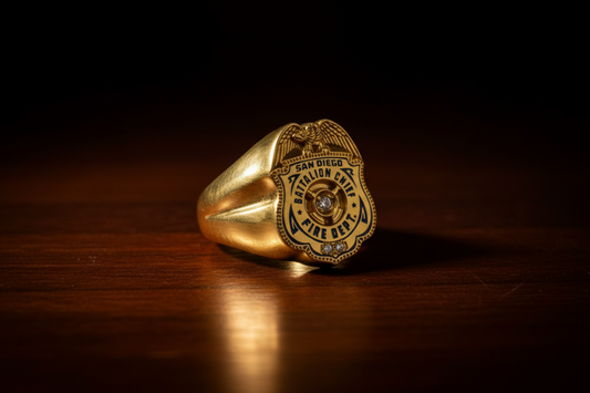 Gold firefighter badge ring resting on a wooden surface, featuring a San Diego Battalion Chief Fire Dept emblem with engraved details and a polished finish.