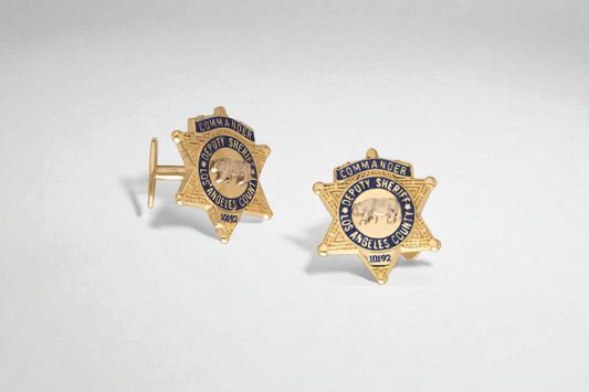 Gold cufflinks shaped like Los Angeles County Deputy Sheriff badges with blue enamel details and engraved commander title.