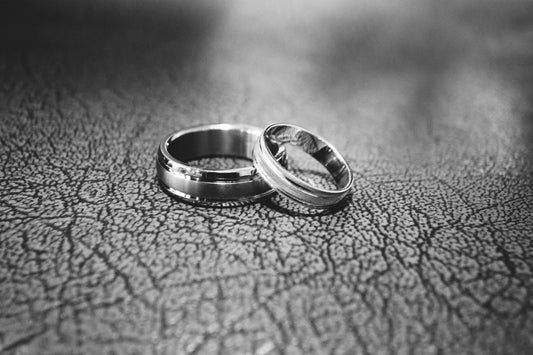 Close-up of two matching silver wedding bands with a brushed and polished finish, resting on a textured leather surface.