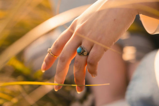 Close-up of a hand wearing a turquoise statement ring, with a gold band on the other finger, set against a soft, natural background.