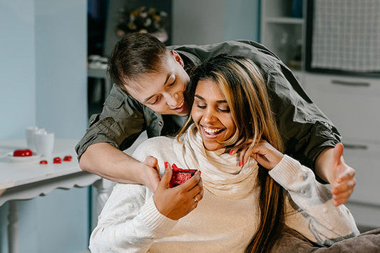 Couple enjoying a joyful moment together, with the woman smiling and holding a gift, while the man embraces her from behind.